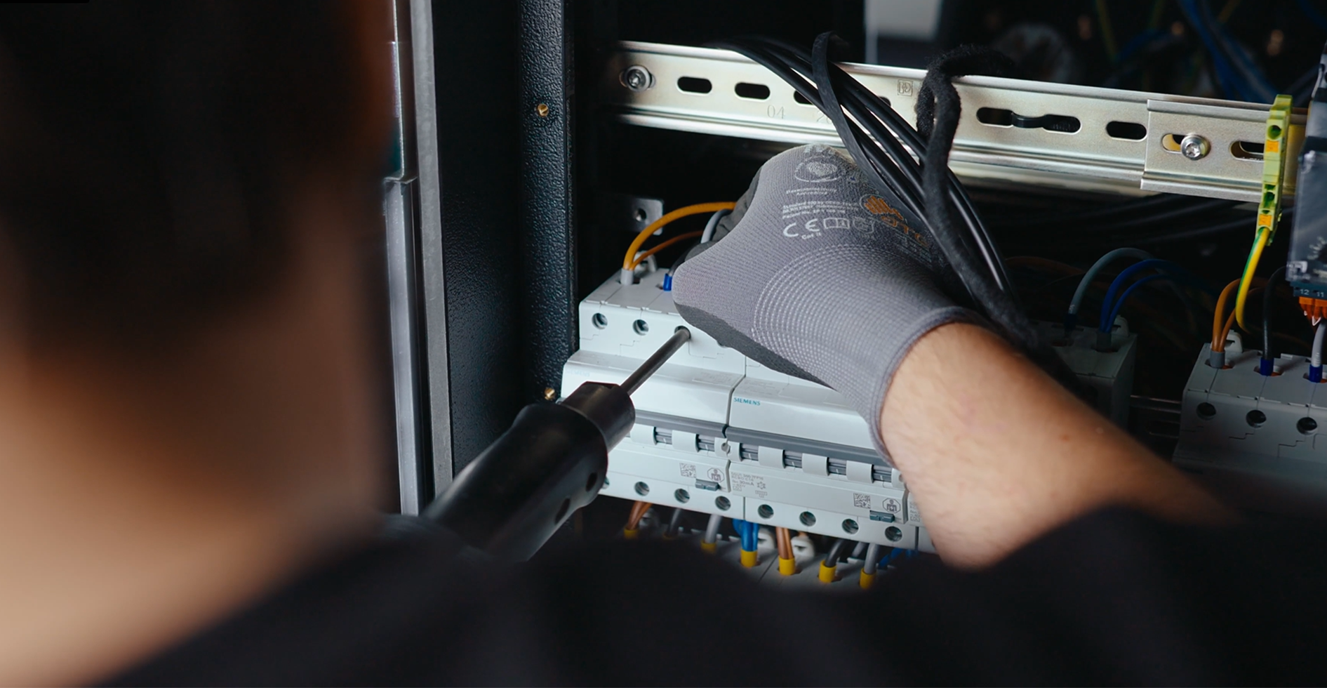 Gloved technician wiring Siemens protection devices inside a distribution unit